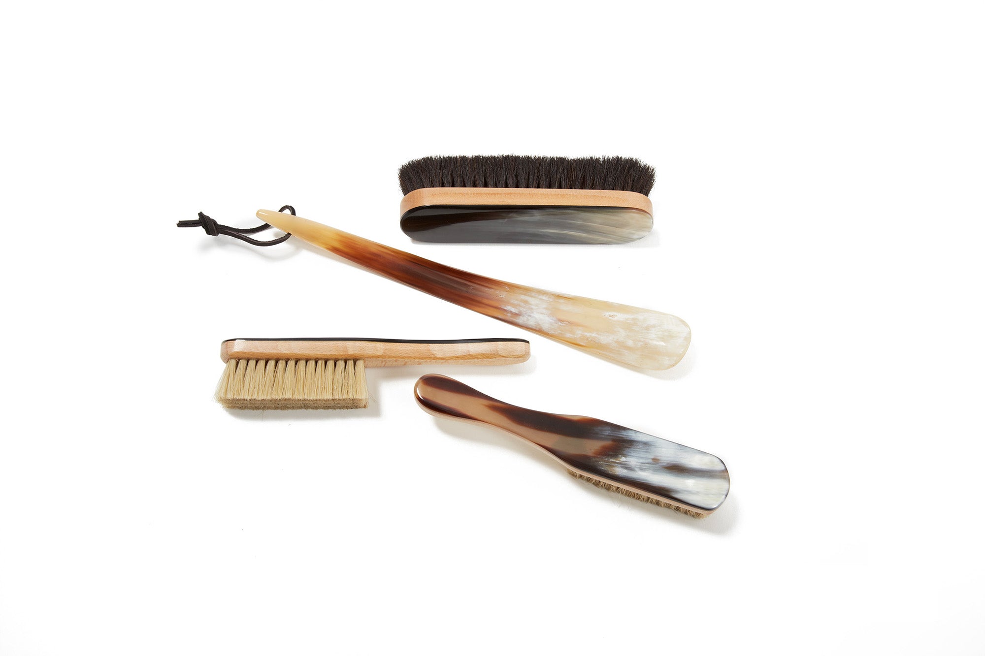 Three brushes and a shoehorn with horn handles arranged on a white background.