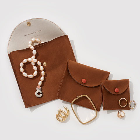 Three Sizes Of Brown Suede Jewelry Pouches With Jewelry On Top Of Them