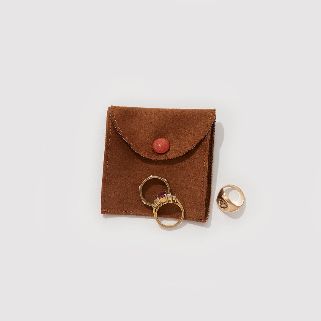 A Brown Suede Jewelry Pouch With Some Rings On Top Of It