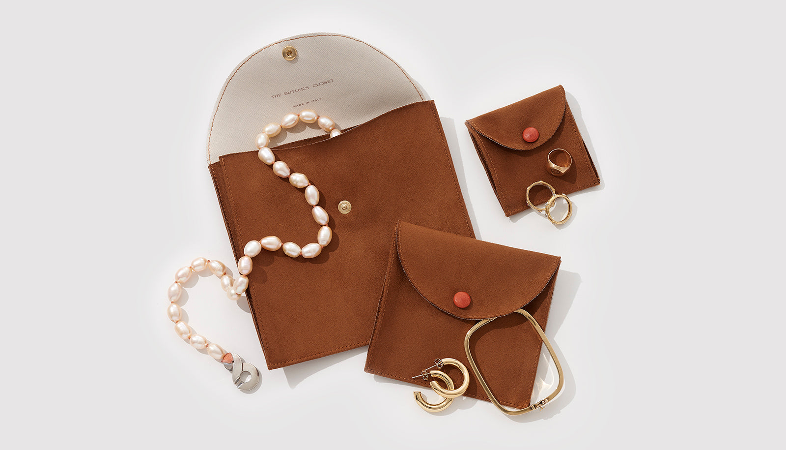 Three Elegant Italian Suede Jewelry Pouches Of Different Sizes With A Necklace, Some Earrings And Some Rings On Top Of Them