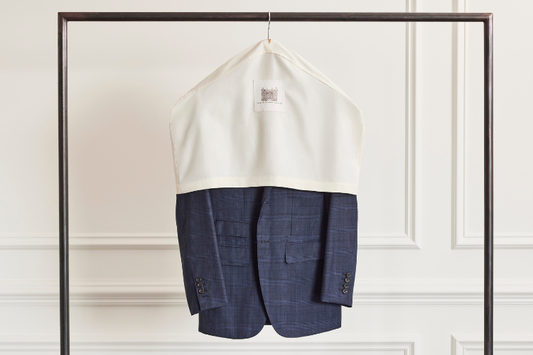 A navy suit coat hanging on a rack, partially covered by a white garment bag