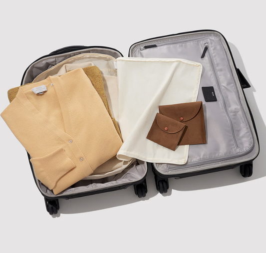Open suitcase with neatly folded clothes, a fabric pouch, and two small brown leather cases arranged inside.