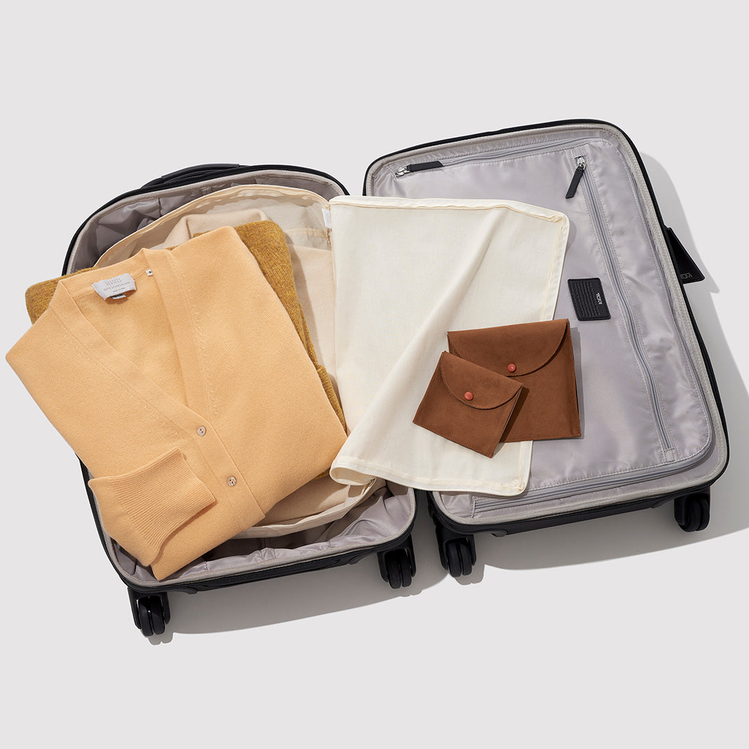 An Open Suitcase With Some Clothing Inside It And Two Brown Suede Jewelry Bags On Top Of It