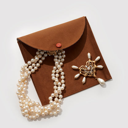 A Brown Suede Jewelry Pouch With A Necklace And A Brooch On Top Of It