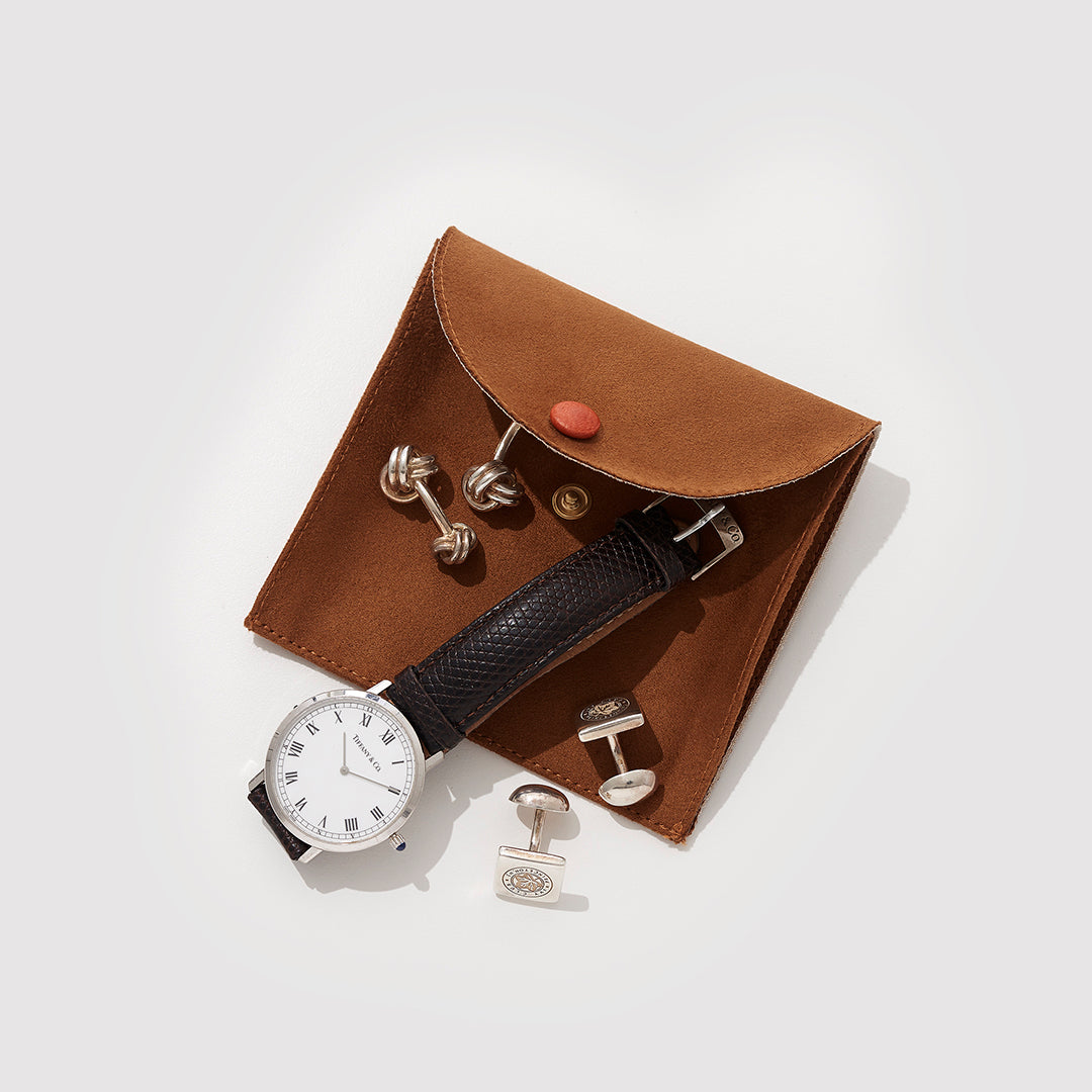 A Brown Suede Jewelry Pouch With A Watch And Some Cufflinks On Top Of It